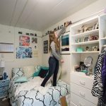 A student arranges photographs on the wall of her dorm room.