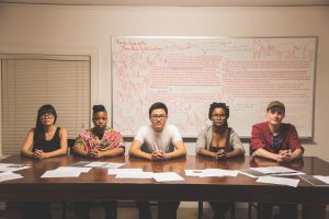 Photo of Alex Jen, Williams Class of 2018, center, who curated the exhibition "No Agenda" in the Williamstown Municipal Building with visiting art professors, from left, Nicole Maloof, Allana Clarke, Ilana Harris-Babou and Zak Arctander. Not pictured is visiting art professor Kim Faler. All five are seated in front of "For the Office of the Town Clerk of Williamstown," 2017. Dry erase marker on white board, 46.5 x 94 in.
