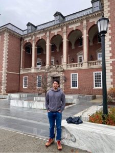 A man in sweatshirt and jeans stands in front of the library at Williams College.