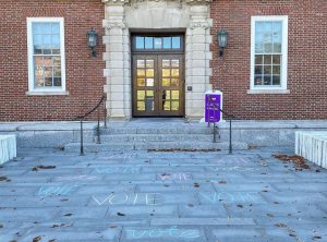 The word "vote" is written in chalk across the walkway in front of Sawyer Library.