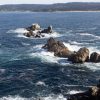Blue ocean waters are seen swirling around rocks on the coast.
