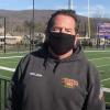 Williams College groundkeeper Jimmy Menard wears a black face mask and stands in front of the football field.