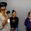 A photo of students in Professor Christorpher Goh's Introductory Chemistry course using virtual reality to learn about molecules. The student in the foreground wears black goggles and is looking up at the ceiling.