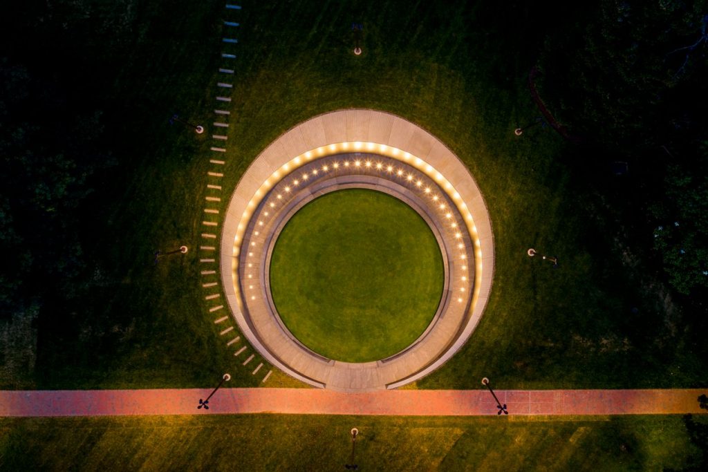 An aerial view of the Memorial to Enslaved Laborers at the University of Virginia shows a circular brick wall lined by lights all around, with a grassy lawn in the middle.