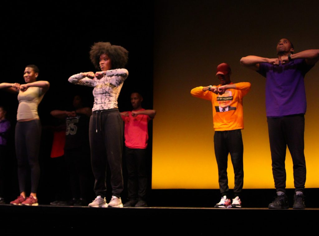 A group of men and women perform a step routine on stage.